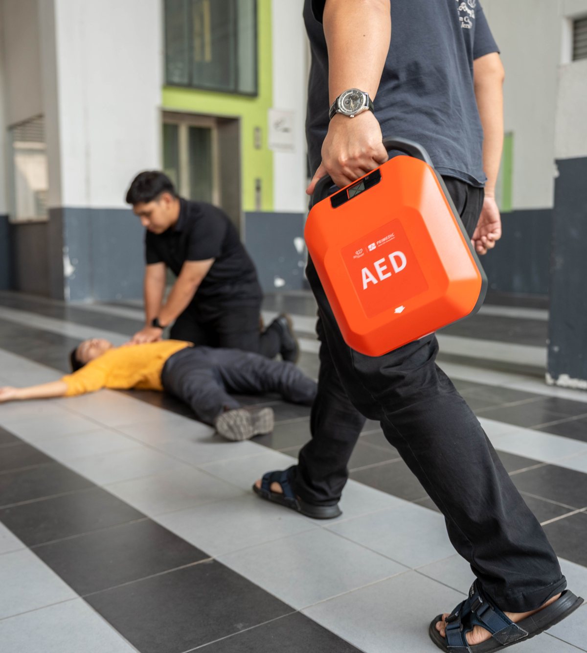 Rescuer bringing a MyHeart Primedic S-Series AED while a first aider gives CPR